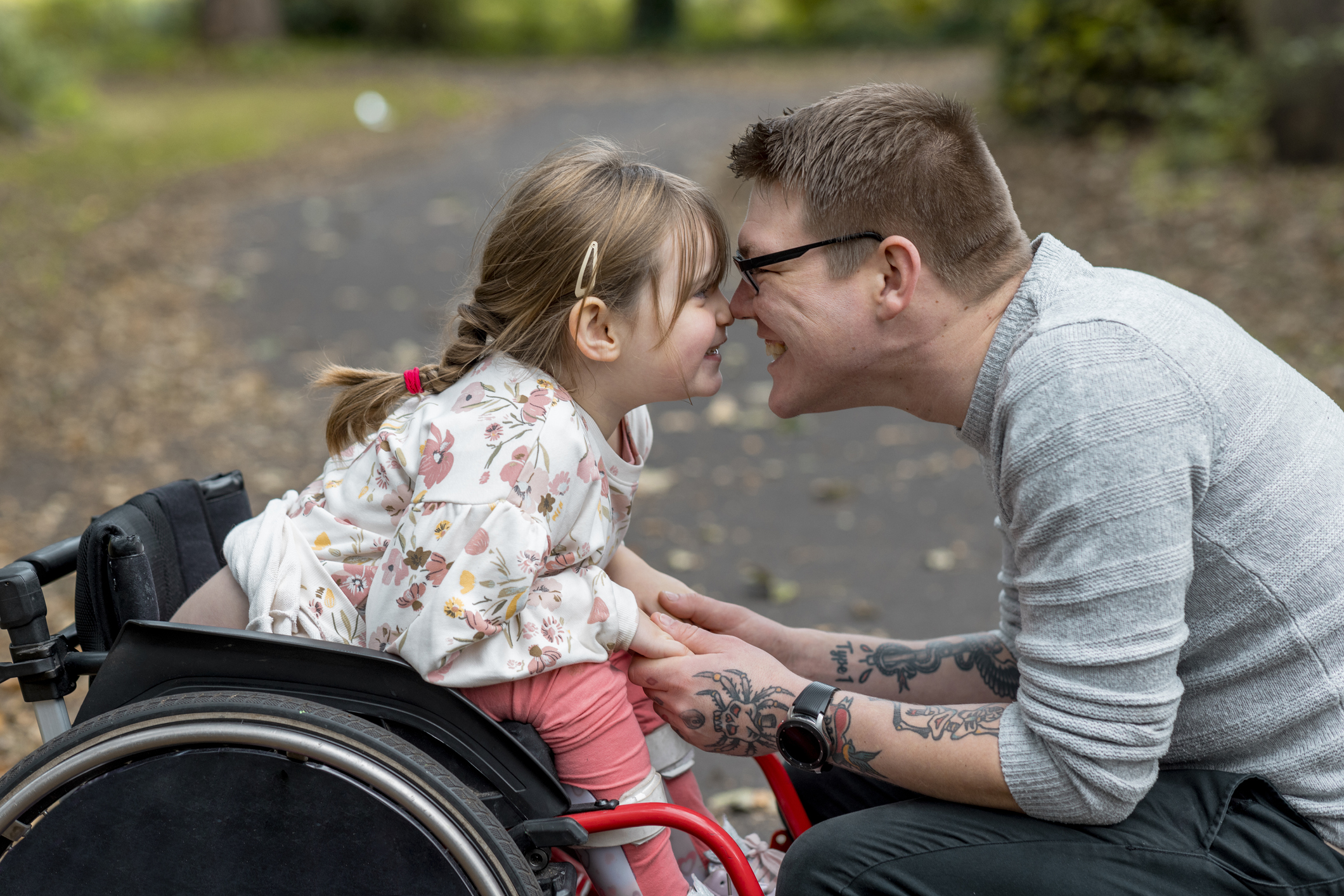 Father, nose to nose with his young daughter who uses a wheelchair.